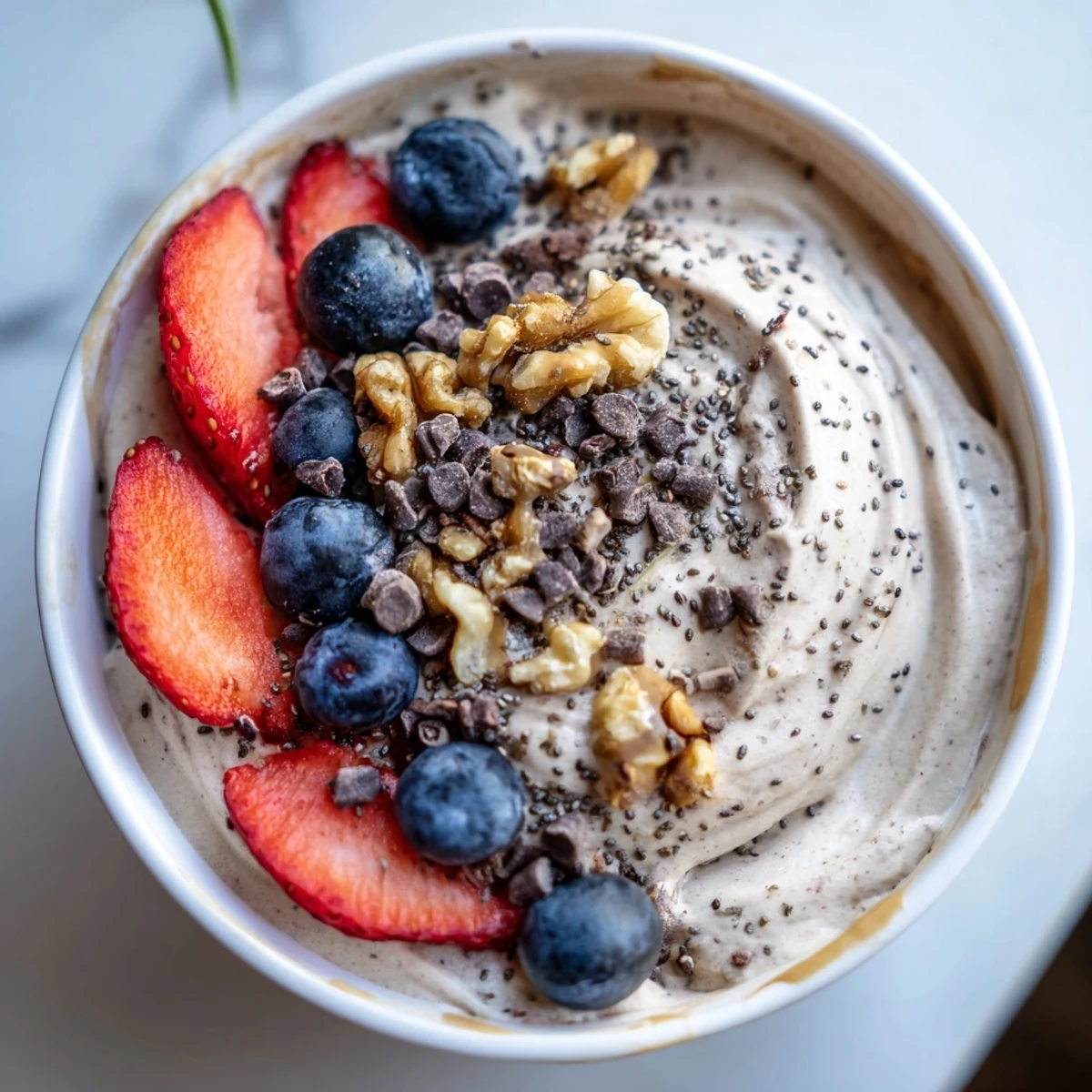 A close-up of a delicious Protein Ice Cream Bowl, ready to be topped with chocolate chips and nuts.
