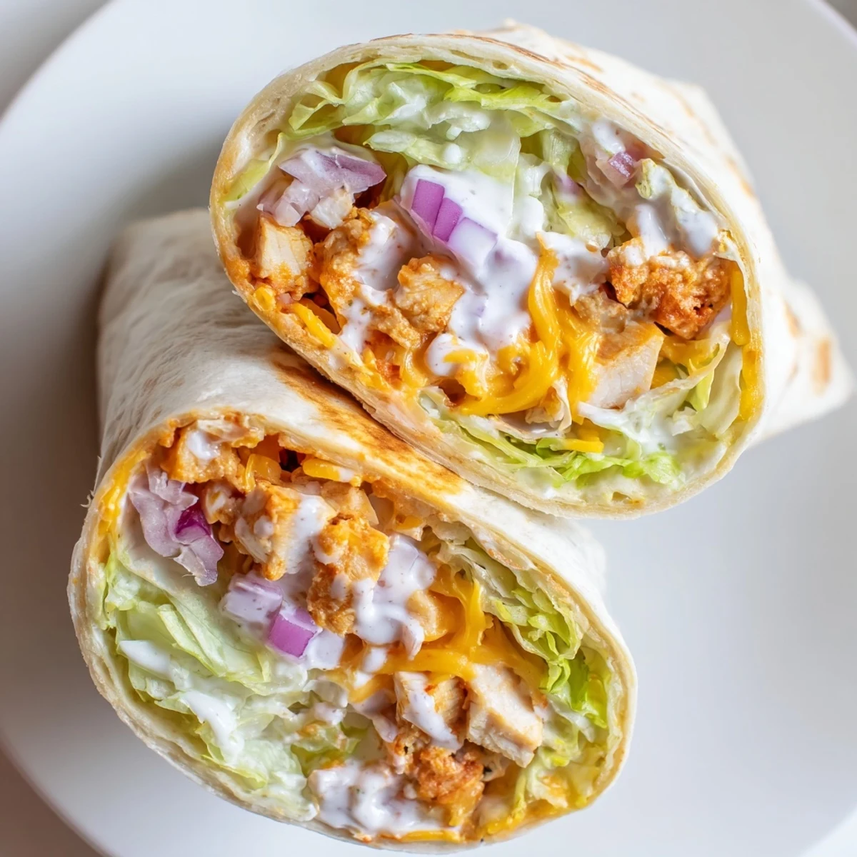 A handheld Buffalo Ranch Chicken Wrap sliced in half to show spicy chicken, crunchy lettuce, and melty cheese inside warm flour tortillas.