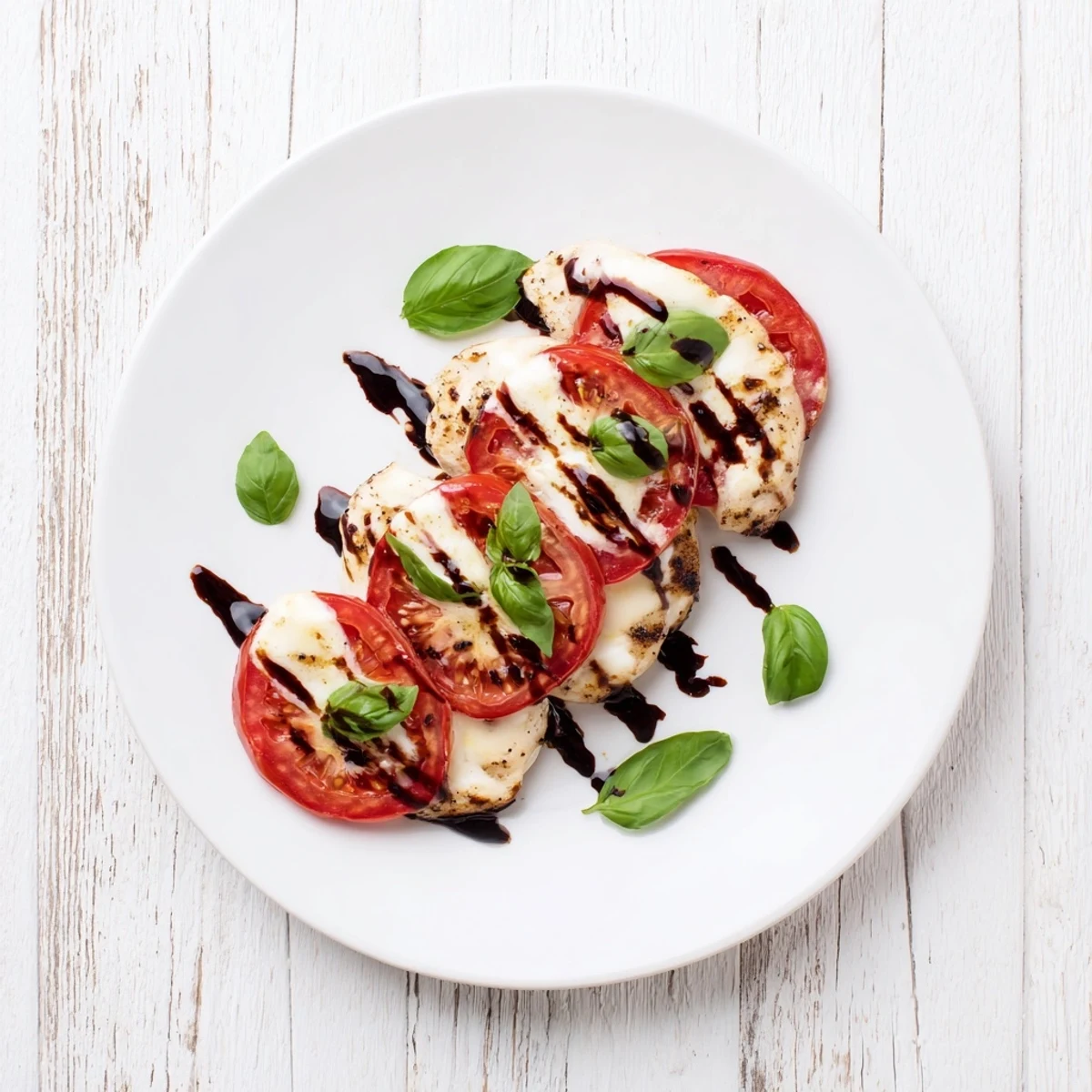 Golden-brown Caprese Chicken Skillet topped with melted mozzarella, ripe tomato slices, and fresh basil, drizzled with balsamic glaze on a rustic plate.