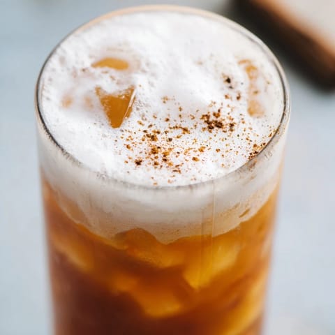 Two glasses of iced chai tea with cold foam garnished with cinnamon, served over ice cubes on a sunny table.  