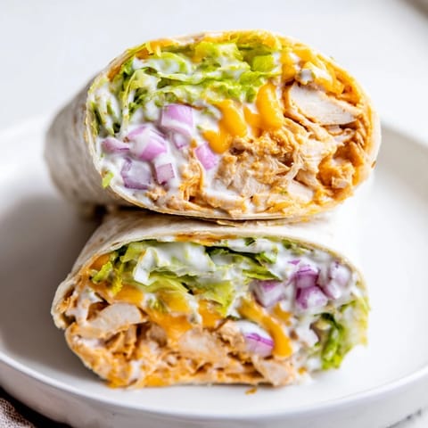 Freshly assembled Buffalo Ranch Chicken Wrap with shredded chicken, crisp romaine, and melted cheddar in a toasted tortilla, drizzled with extra ranch.