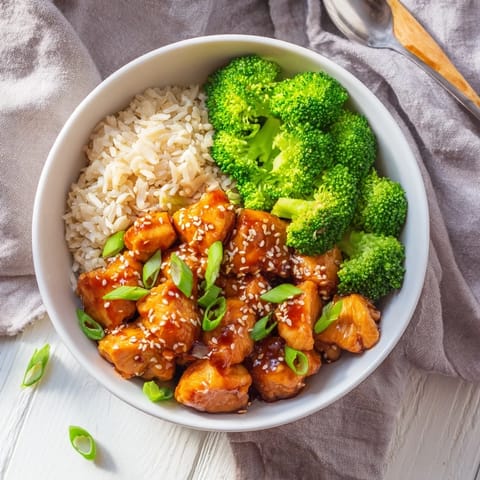 A top-down view of a vibrant Sweet Chili Chicken Bowl with saucy chicken, steamed broccoli, and a sprinkle of sesame seeds on fluffy rice.